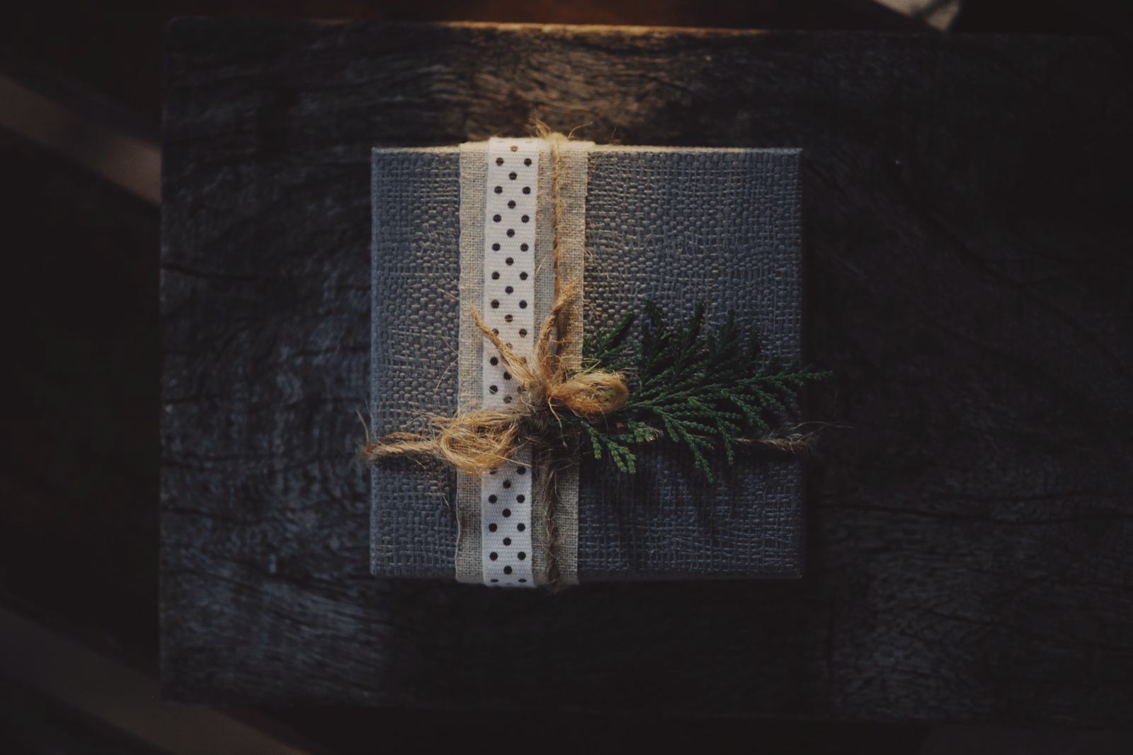 Elegant rustic gift box with polka dot ribbon and fern decoration on a dark wooden background.